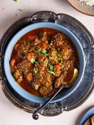 A bowl of beef masala in a tray on a flat surface.