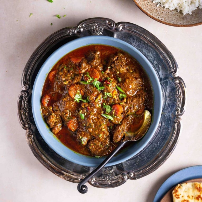 A bowl of beef masala in a tray on a flat surface.