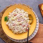 chicken salad with grapes in a yellow bowl with salad spoon and napkin on a flat surface.