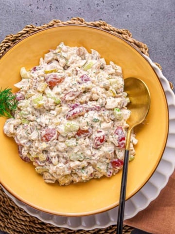 chicken salad with grapes in a yellow bowl with salad spoon and napkin on a flat surface.