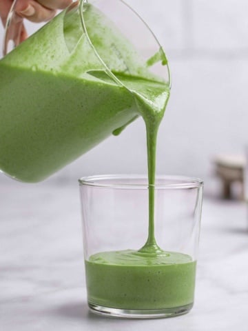 banana and spinach smoothies getting poured into a cup.
