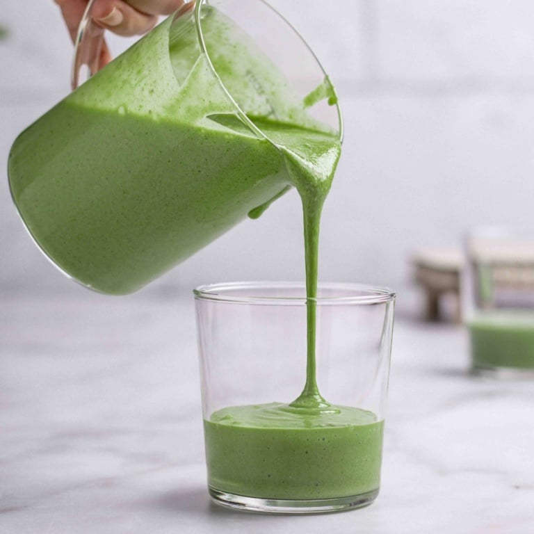 banana and spinach smoothies getting poured into a cup.