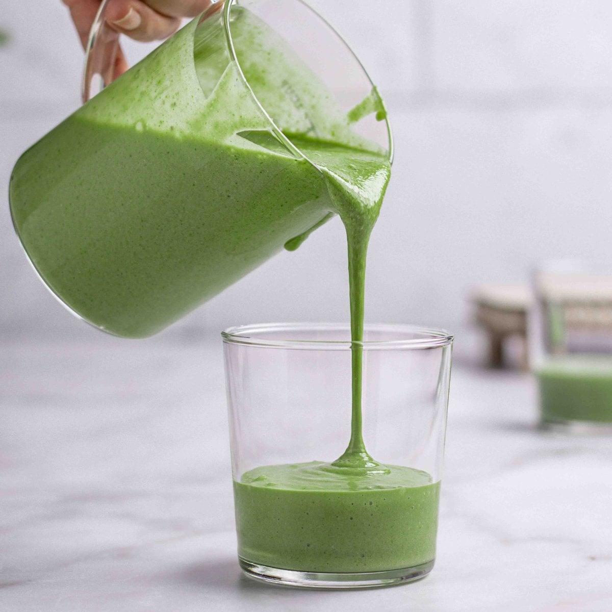 banana and spinach smoothies getting poured into a cup.