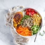 quinoa bowl topped with grilled mangoes, carrots, tomatoes, corn, and dill.
