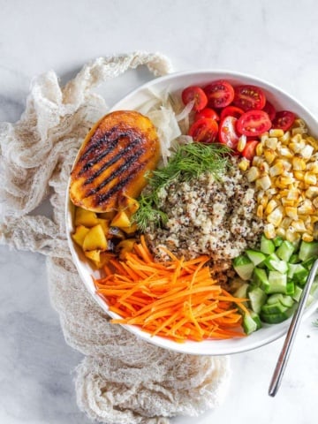 quinoa bowl topped with grilled mangoes, carrots, tomatoes, corn, and dill.