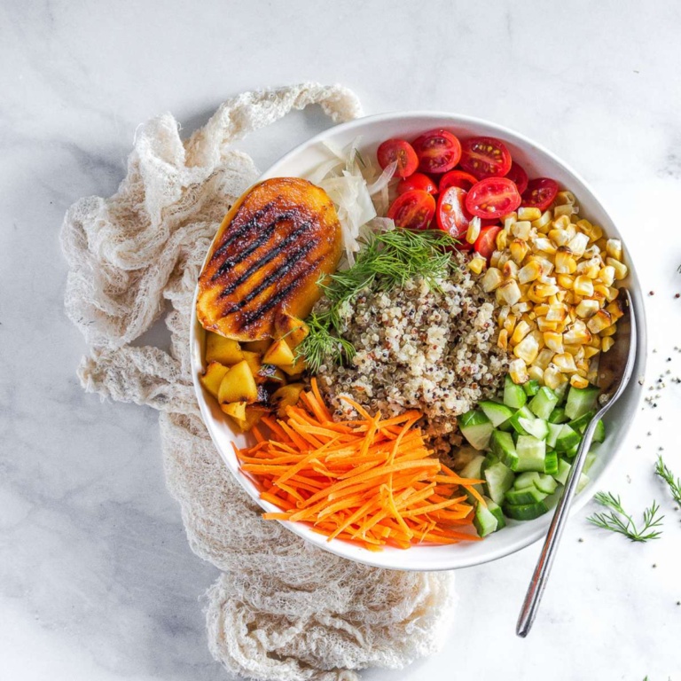 quinoa bowl topped with grilled mangoes, carrots, tomatoes, corn, and dill.