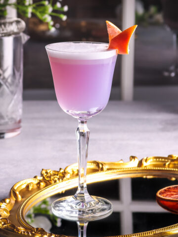 a photo of grapefruit gin cocktail on a glass tray garnished with grapefruit twist.