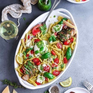 Chicken caprese pasta salad with basil pesto in a serving platter.