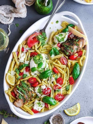 Chicken caprese pasta salad with basil pesto in a serving platter.