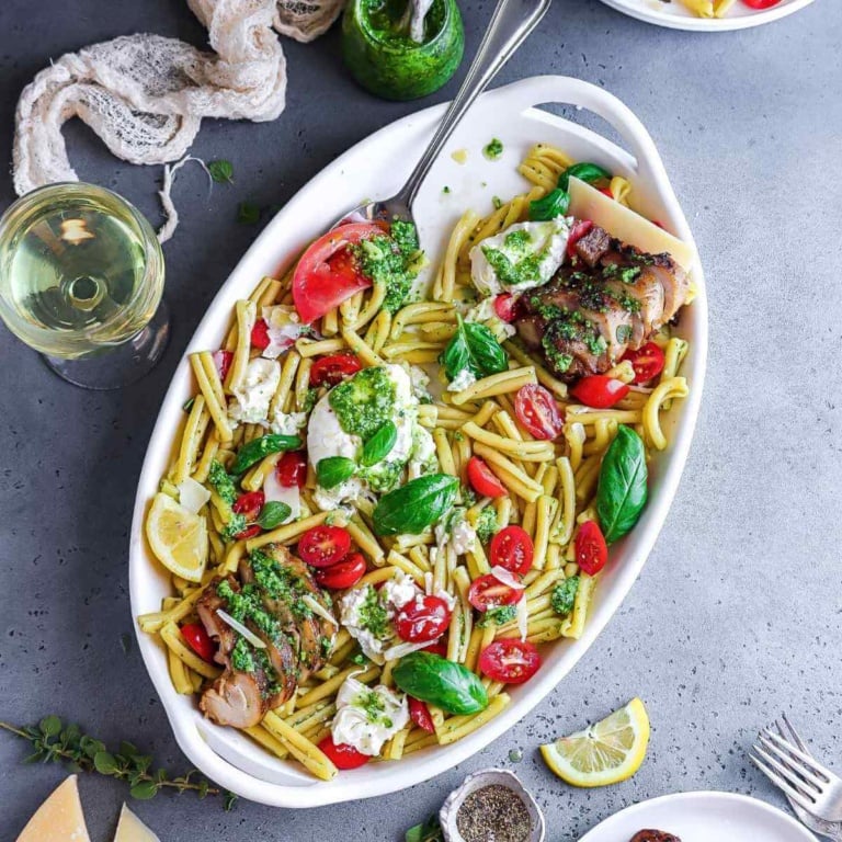 Chicken caprese pasta salad with basil pesto in a serving platter.