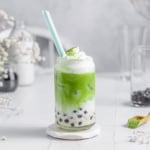 green milk tea in a glass cup with frothed milk and dusted with matcha powder.