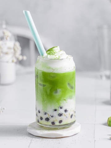 green milk tea in a glass cup with frothed milk and dusted with matcha powder.