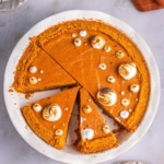 Sweet potato pie with graham cracker crust topped with marshmallow fluff on a pie dish.