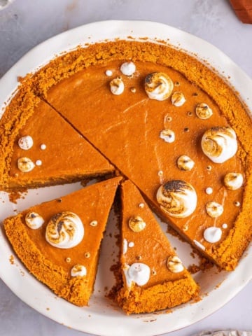 Sweet potato pie with graham cracker crust topped with marshmallow fluff on a pie dish.