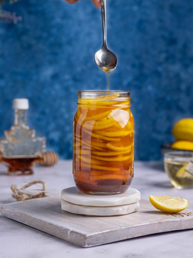 Honeyed lemons in a jar showing the syrup using a spoon.