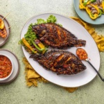whole tilapia fish air fried and served alongside spicy pepper sauce and sautéed bell pepper vegetables.