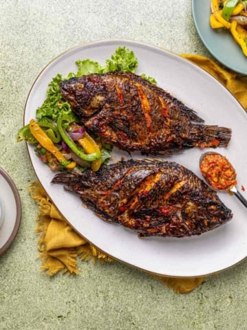 whole tilapia fish air fried and served alongside spicy pepper sauce and sautéed bell pepper vegetables.
