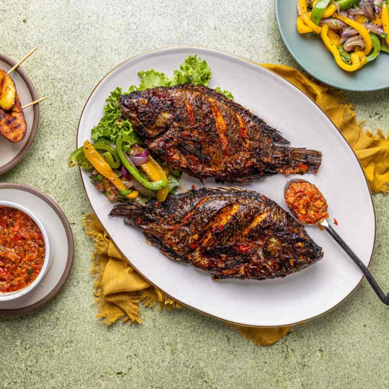 whole tilapia fish air fried and served alongside spicy pepper sauce and sautéed bell pepper vegetables.
