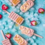 Frozen popsicles with wedged strawberries on a flat surface.