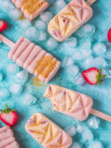 Frozen popsicles with wedged strawberries on a flat surface.