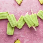 Homemade pineapple coconut popsicles on a pink background.