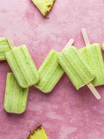 Homemade pineapple coconut popsicles on a pink background.