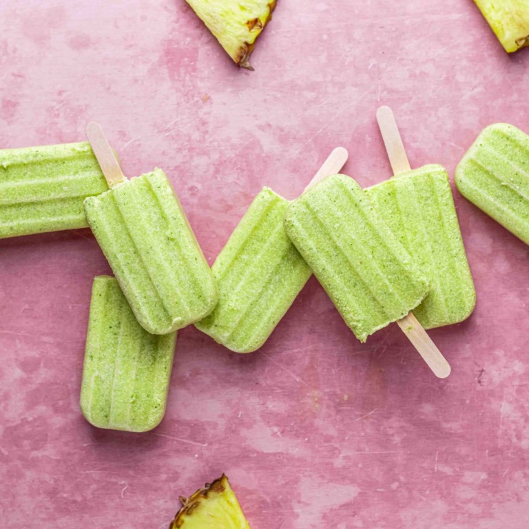 Homemade pineapple coconut popsicles on a pink background.