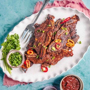 Flanken beef short ribs on a platter with green onion and sauce.