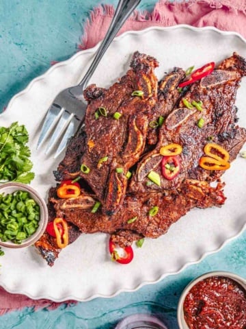 Flanken beef short ribs on a platter with green onion and sauce.