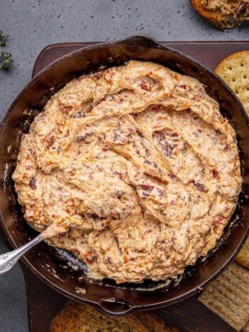 Baked Boursin dip with crackers on a wooden board.