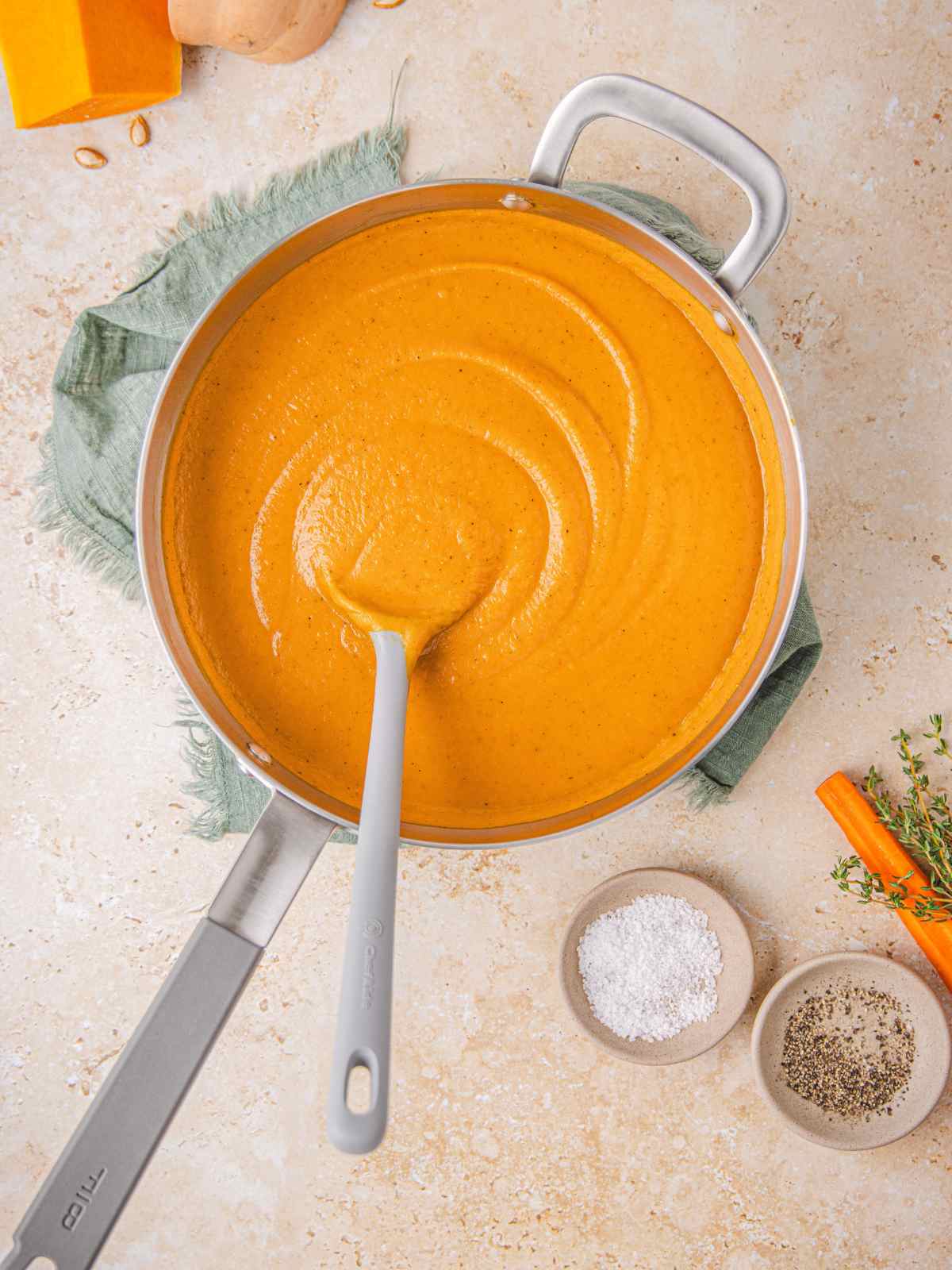 A pot of carrot and squash soup in a sauté pot with spoon.