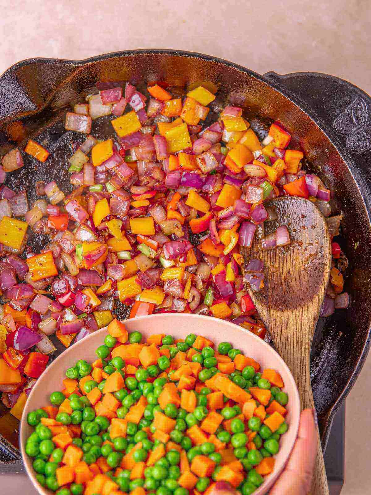 Adding the vegetables into the pan with onion and peppers.