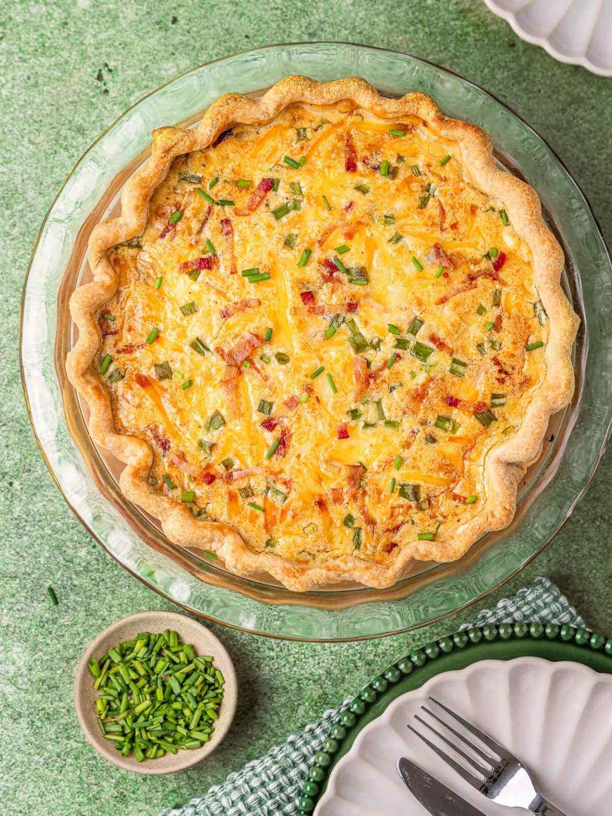 Bacon quiche on a pie dish with serving plates.