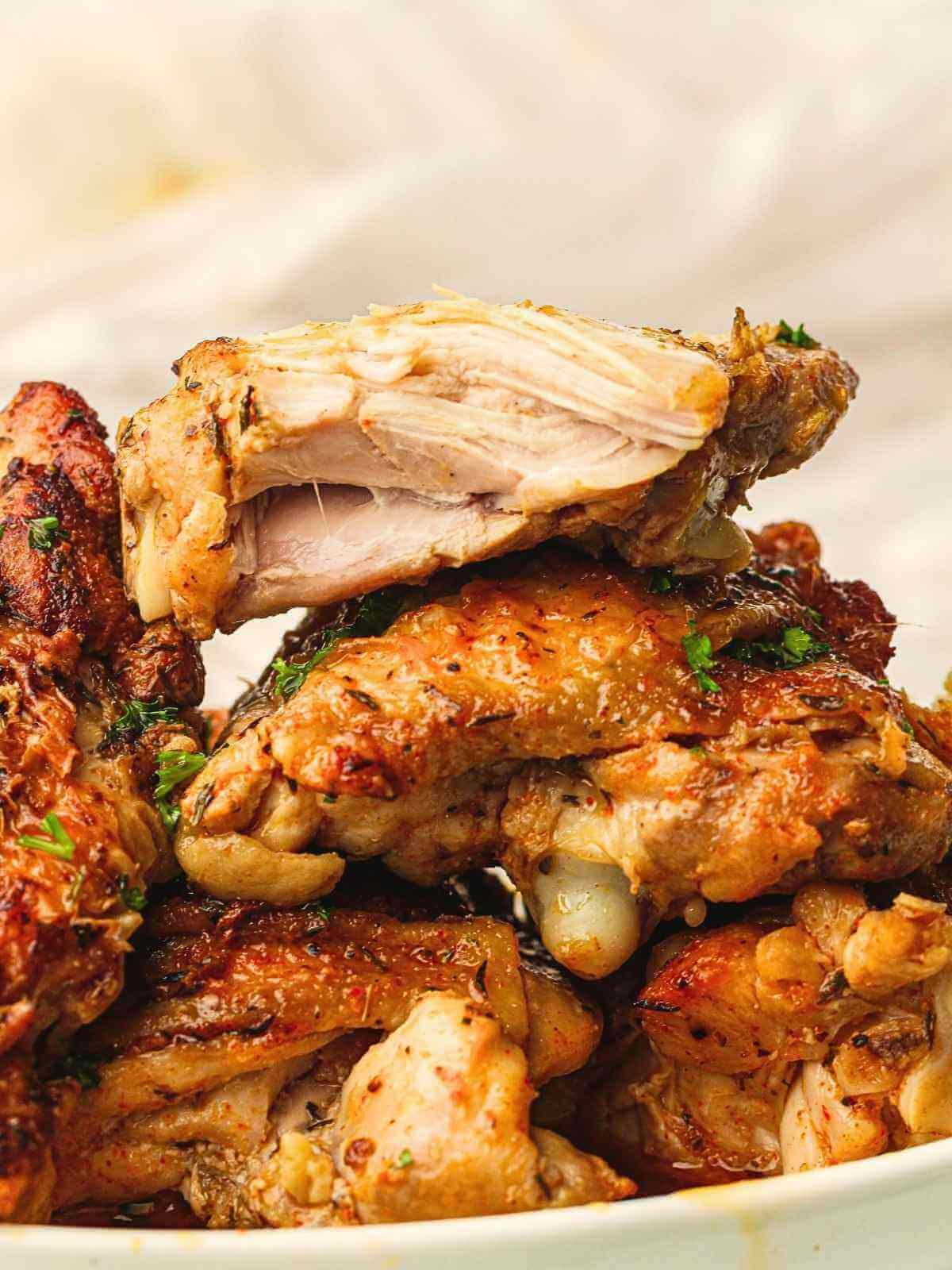 Stack of juicy skin-on, bone-in chicken thighs on a flat plate.